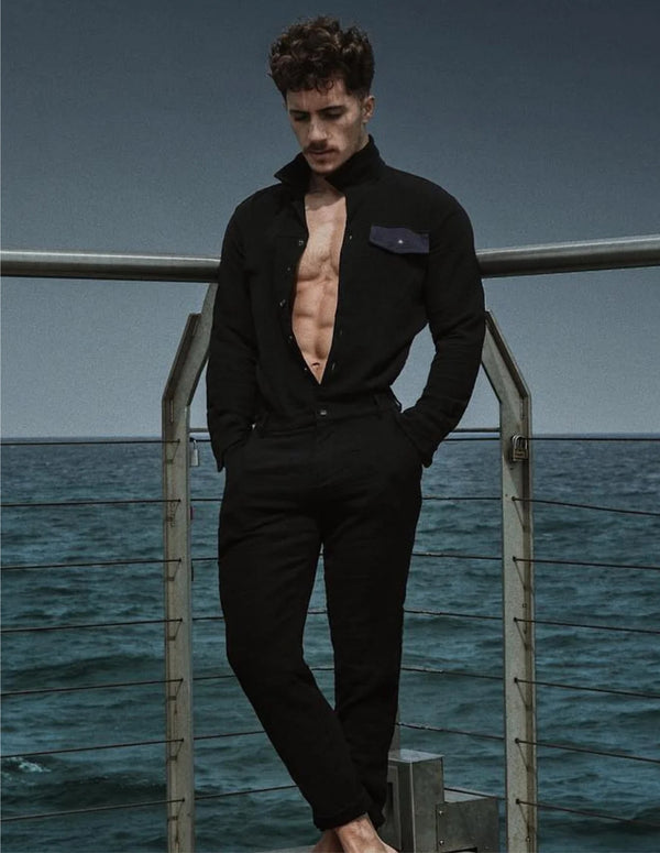 Man in a black outfit standing on a dock with ocean in the background