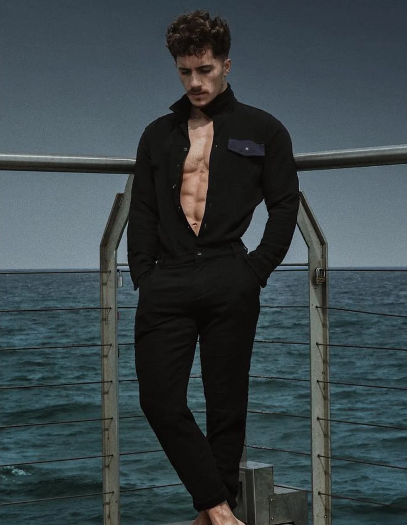 Man in a black outfit standing on a dock with ocean in the background