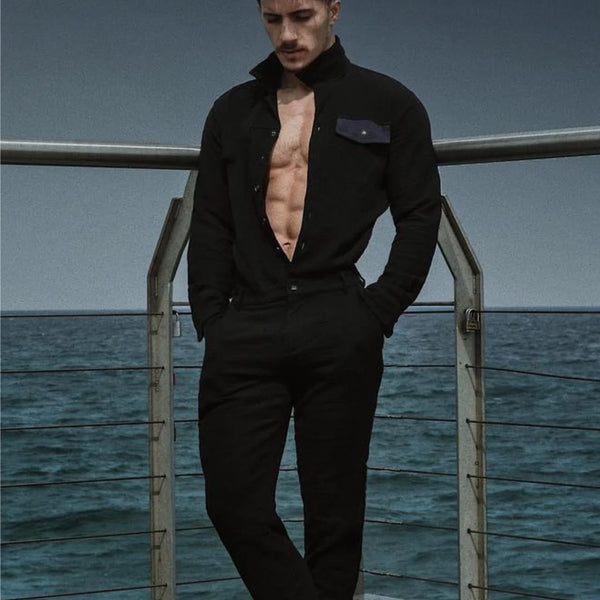 Man in a black outfit standing on a dock with ocean in the background